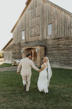 a bride and groom holding hands in front of a barn