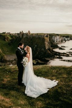 a bride and groom standing on top of a hill next to the ocean with cliffs in the background