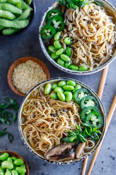 two bowls filled with noodles and vegetables next to chopsticks on a table top