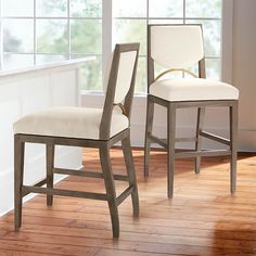 two white chairs sitting on top of a hard wood floor next to a large window