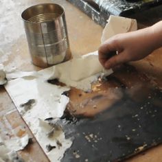 someone is making something out of paper on a table with a can and some other items