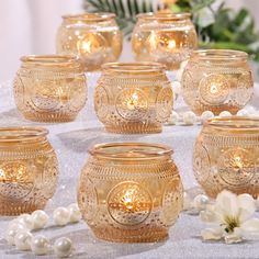 there are many gold glass jars on the table with pearls around them and flowers in the background