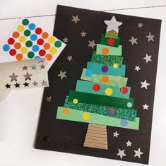 a christmas tree made out of construction paper on top of a black card with stars and confetti