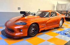 an orange sports car is parked in a garage with checkered flooring on the ground