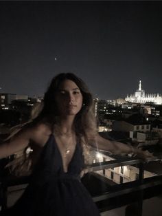 a woman standing on top of a balcony next to a night time cityscape