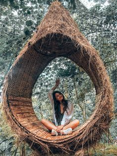 a woman sitting on top of a wooden structure in the middle of a forest with trees