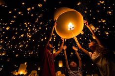 three people releasing lanterns into the sky with their hands in the air at night time