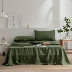 a bed with green sheets and pillows in a white room next to a potted plant