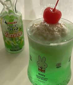 a green drink with a cherry on top next to a bottle of ramune milk