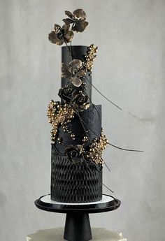 a three tiered cake with black frosting and gold flowers on top is shown