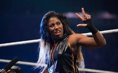 a woman with long hair standing in front of a microphone and making the peace sign