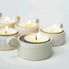 four white tea cups with lit candles in them