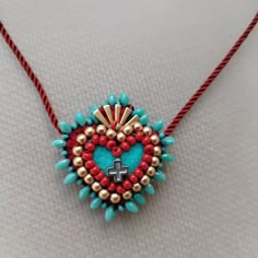 a beaded heart with a cross hanging from it on a red and blue string