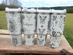 four different styles of travel mugs sitting on a wooden table in front of a grassy field