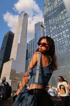 a woman standing in front of tall buildings with her back to the camera and wearing sunglasses