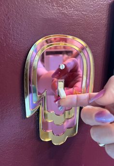 a woman's hand is touching the handle on a pink and gold wall mounted mirror