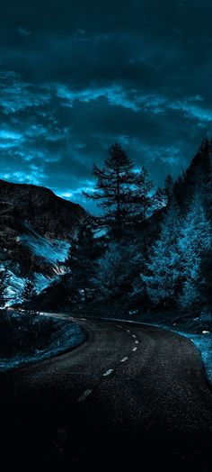 an empty road in the middle of a mountain range with trees on both sides at night