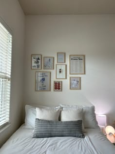 a bed with white sheets and pillows in front of a window filled with framed pictures