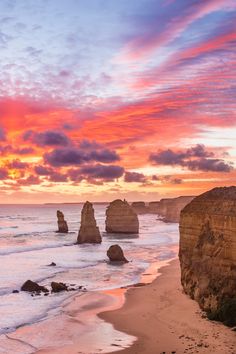 sunset over the ocean with rocks in the foreground and clouds in the sky above