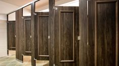 a row of wooden stalls in a bathroom with tile flooring and wall coverings