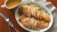 sliced chicken on a white plate next to a bowl of gravy and silverware