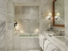 a bathroom with marble walls and flooring has candles lit in the bathtub next to the tub