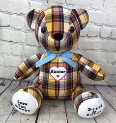 a plaid teddy bear sitting on top of a wooden floor next to a brick wall