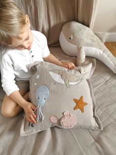 a little boy that is sitting on a bed with a pillow and stuffed animals in front of him