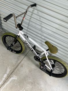 a white and green bike parked in front of a garage door with no wheels on it