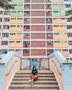 a woman sitting on the steps in front of a tall building with balconies