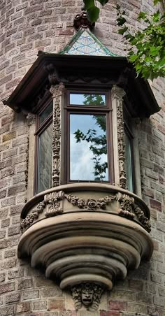 an ornate window on the side of a brick building with green trees in the background