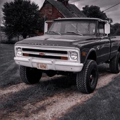 an old pickup truck parked in front of a red brick house on a dirt road