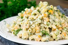 a white plate topped with macaroni salad and garnished with fresh herbs