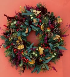 a christmas wreath on a pink wall with berries, pine cones and other holiday decorations