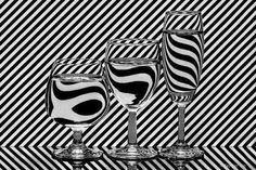 three wine glasses sitting next to each other on a black and white striped tablecloth