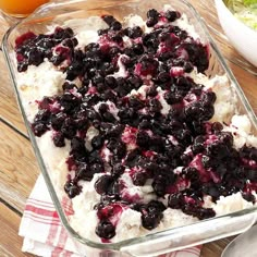 a casserole dish with blueberries and whipped cream in it on a wooden table