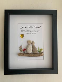 a wedding anniversary gift is displayed in a black frame with two pebbles on it