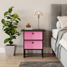 a pink nightstand next to a bed with a plant in it and a lamp on top