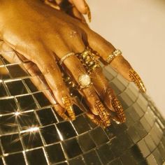 a woman's hand with gold manicures and rings on top of a mirror