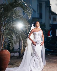 a woman in a wedding dress standing next to a palm tree