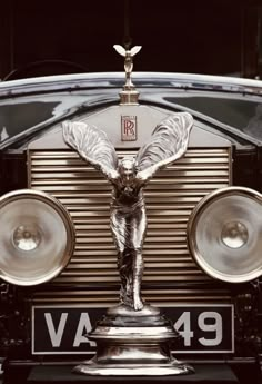 the front end of an antique car with a statue on it's hood and speakers