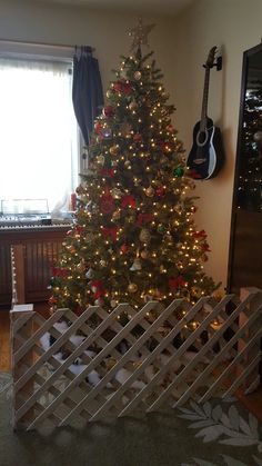 a christmas tree with lights in a living room next to a guitar rack and window