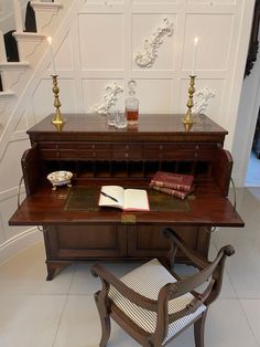 a wooden desk with a book on top of it next to a chair and candle holders