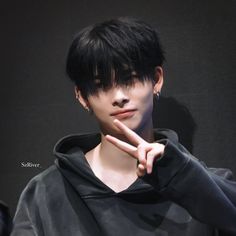 a man with black hair and piercings pointing to the side while wearing a hoodie