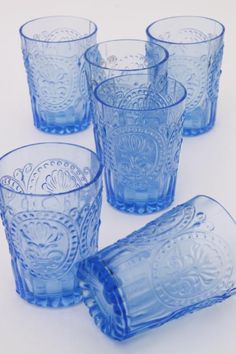 six blue glass tumblers with ornate designs on the rims and sides, all lined up