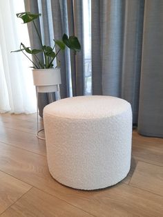 a white round ottoman sitting on top of a hard wood floor next to a window