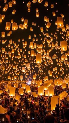 many people are flying lanterns in the sky at night time, with lights on them