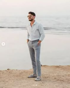 a man standing on top of a sandy beach next to the ocean with his hands in his pockets