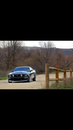 a black car parked on the side of a dirt road next to a wooden fence