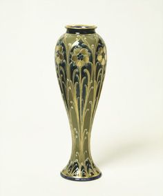 a green vase with yellow flowers on the bottom and black trim around the top, against a white background